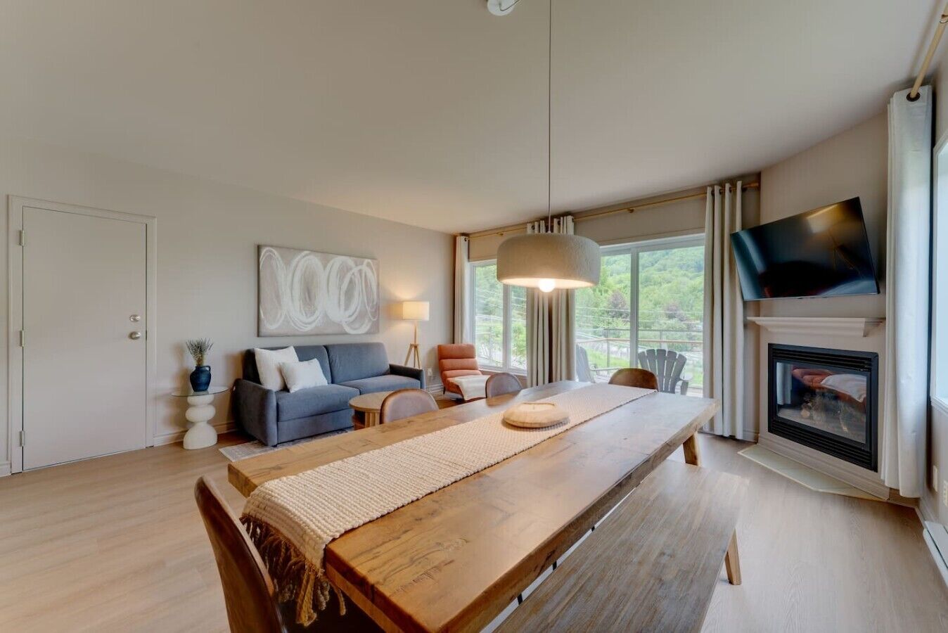 A modern living room with a wooden dining table, a sofa, a TV, and a fireplace.