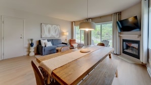 A modern living room with a wooden dining table, a sofa, a TV, and a fireplace.