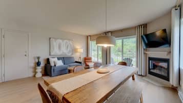A modern living room with a wooden dining table, a sofa, a TV, and a fireplace.