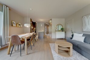 A modern living room with a dining area, a grey sofa, a round coffee table, and a hallway leading to a kitchen. - E201-Condo ski in ski out ~velo in velo out (Bromont)