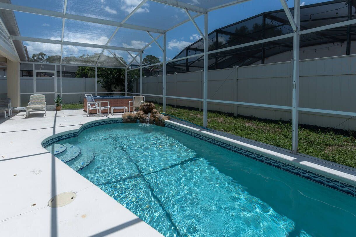 An outdoor swimming pool with a glass enclosure, surrounded by a white fence and a grassy area.