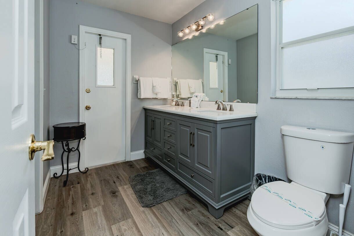 A bathroom with a gray vanity, white fixtures, a large mirror, and a toilet.