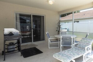 Ein überdachter Patio-Bereich mit Grill, Tisch und Stühlen sowie einer Liege.