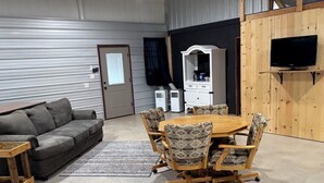 A room with a gray sofa, a wooden dining table with patterned chairs, a white cabinet, and a TV mounted on a wooden wall. - Lake house minutes from the boat dock w/attached garage for boats or vehicles (Foss)