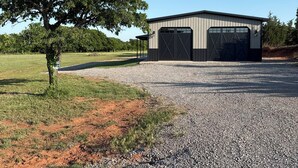 A building with a large tree in front, a gravel driveway, and a clear blue sky. - Lake house minutes from the boat dock w/attached garage for boats or vehicles (Foss)