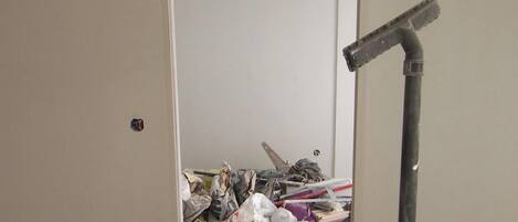 A room with a door leading to a cluttered area with various items and a vacuum cleaner.