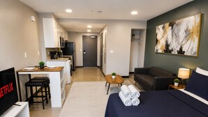 A hotel room with a bed, a desk with a chair, a TV, a sofa, and a painting on the wall. - The Foundry Studio | Downtown Retreat St3 (Birmingham)