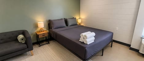 Habitación de hotel con cama, sofá, mesita de noche, lámpara y un calentador de pared.