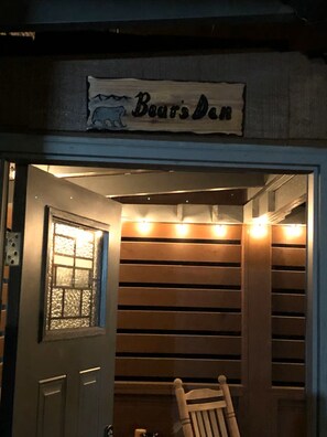 Eine Tür mit einem Schild, auf dem 'Bears Den' steht, ein Holzstuhl und ein Fenster mit einer Sandstrahlmusterung.