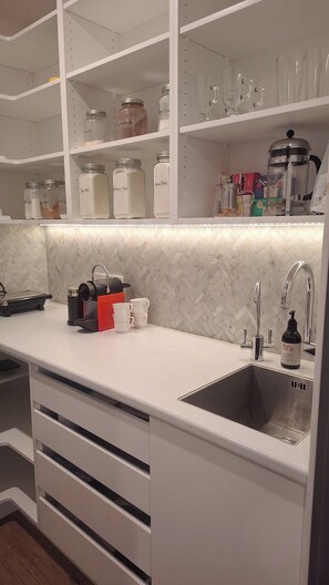 A modern kitchen with white cabinetry, a stainless steel sink, and a coffee maker on the countertop. - Luxury Hilltop Retreat: Hot Tub & Panoramic Views (Waikanae)