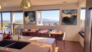 Een moderne keuken met een centraal eiland, een eethoek met een houten tafel en grote ramen met uitzicht op een stadsbeeld.