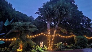 Een tuin met een houten omheining, sfeerverlichting en diverse planten.