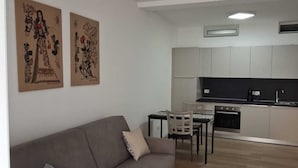 A modern living room with a grey sofa, a dining table with chairs, and a kitchen in the background. - 15 minutes from Taormina, 20 meters from the sea: La Casa di Lucio - I Pupi Apartment (Nizza di Sicilia)