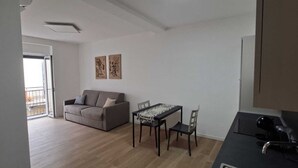 A modern living room with a sofa, dining table, and chairs, a balcony with a railing, and artwork on the wall. - 15 minutes from Taormina, 20 meters from the sea: La Casa di Lucio - I Pupi Apartment (Nizza di Sicilia)