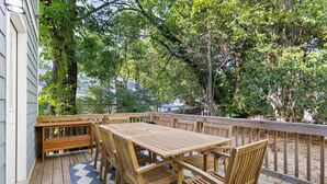Un terrazzo in legno con tavolo e sedie, circondato da un parapetto in legno e alberi.