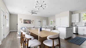 Una cucina moderna con mobili bianchi, una lavastoviglie in acciaio inossidabile e un'area pranzo con tavolo e sedie in legno.