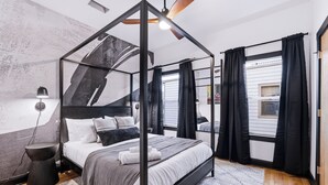 Un dormitori modern amb un llit amb cortines, una taula auxiliar, una làmpada i vista a l'exterior.