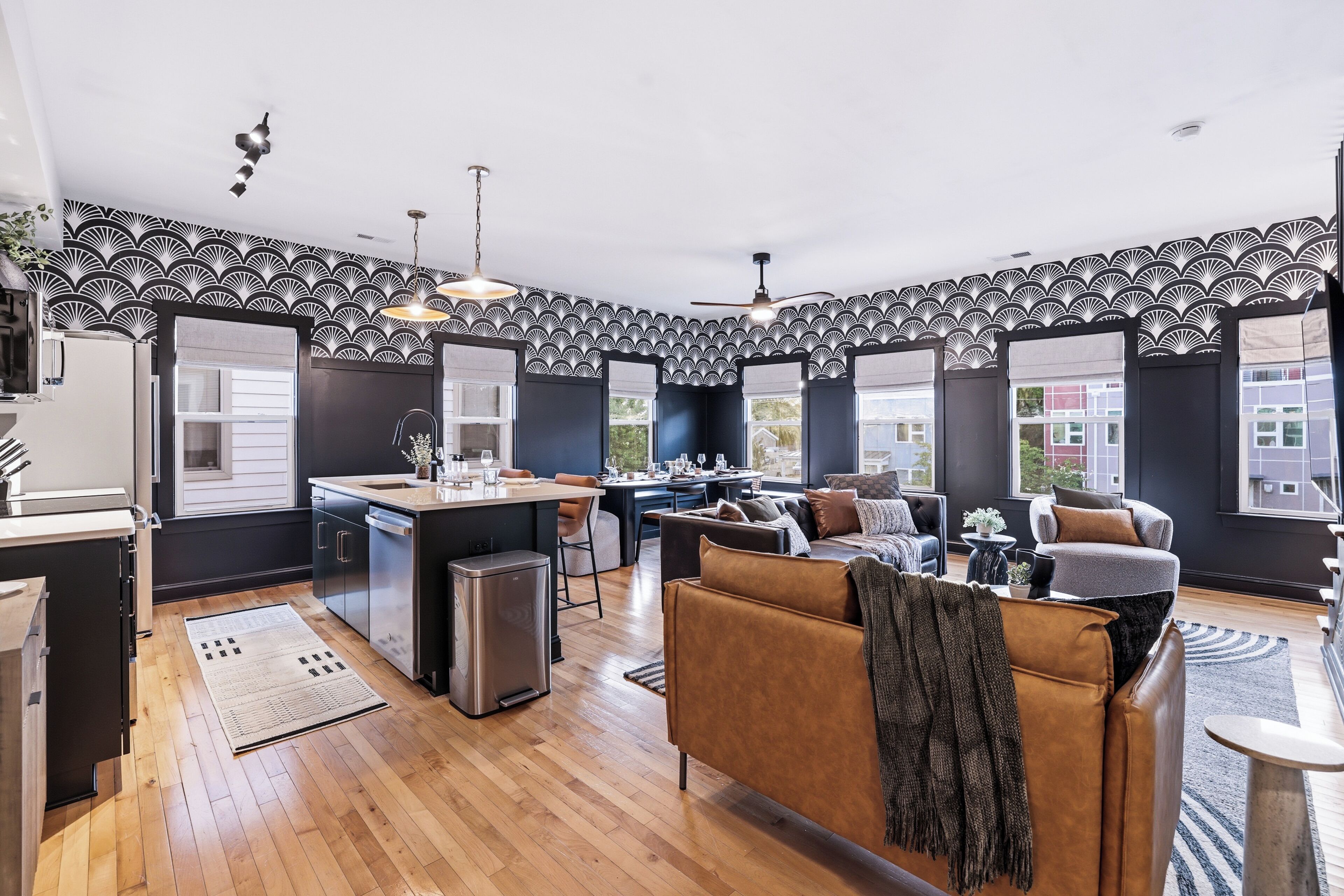 A modern kitchen with a central island, a dining area with a sofa and table, and a living room with a large window.