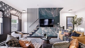 Un saló modern amb una escala, un televisor de pantalla plana i un mural abstracte gran a la paret.