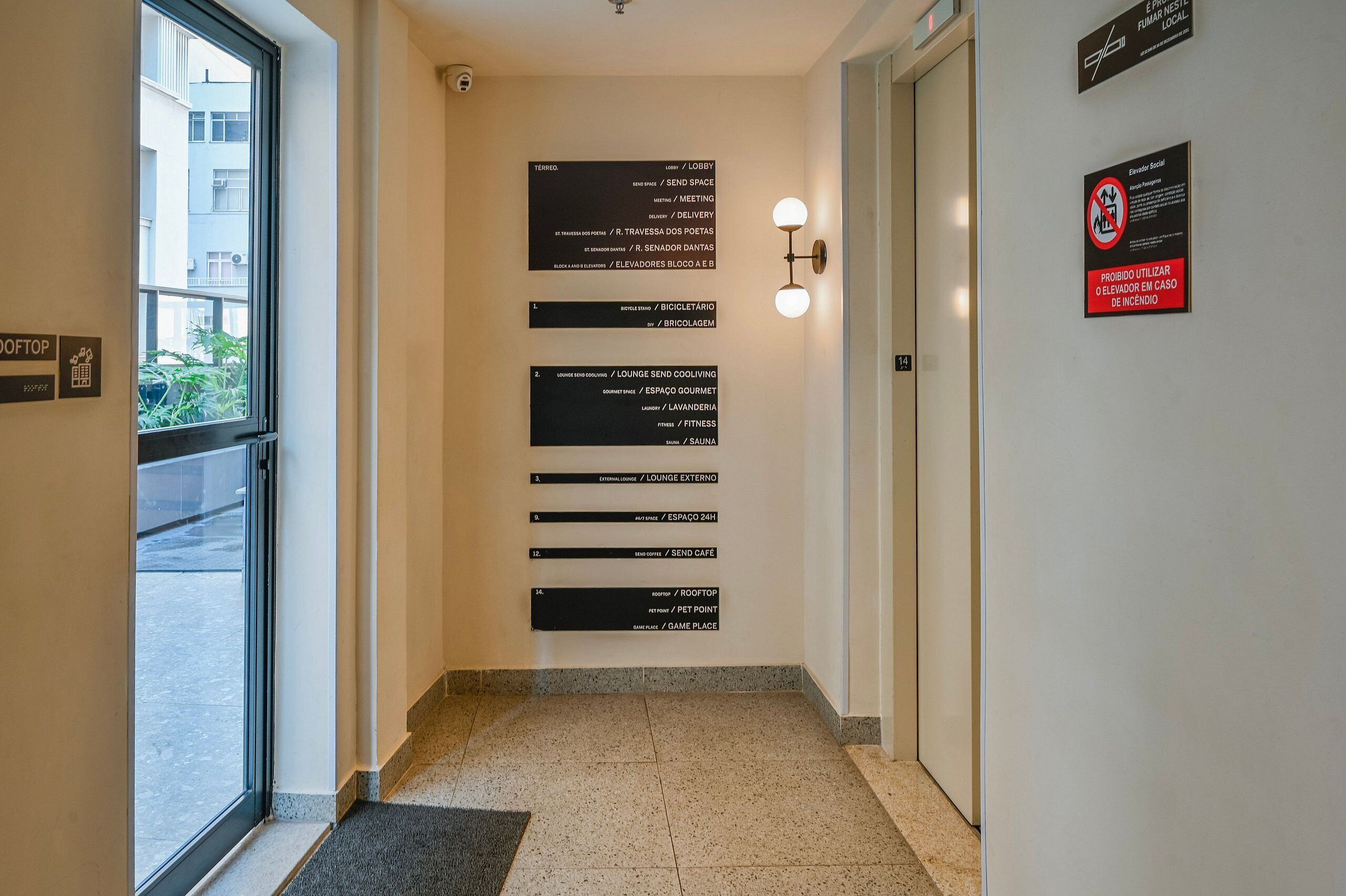 Un couloir avec des panneaux indicateurs, une porte et un luminaire fixé au mur.