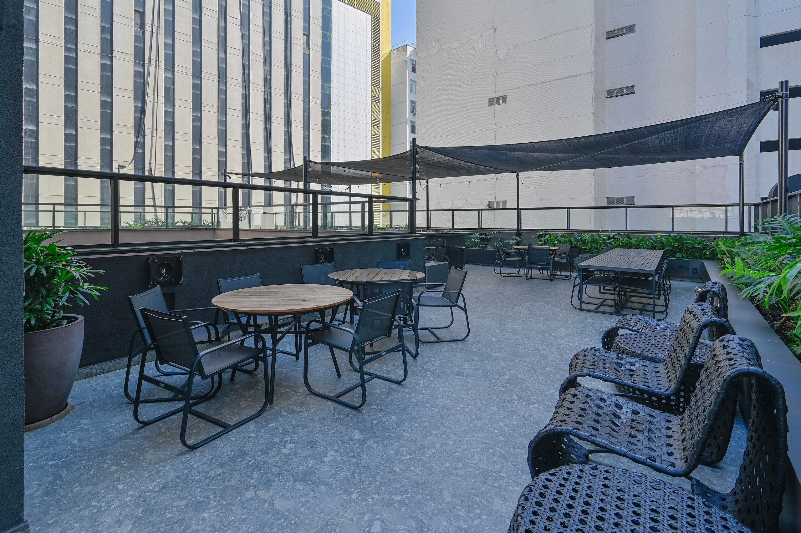 Une terrasse extérieure avec des tables et des chaises rondes, un auvent et des plantes en pot.