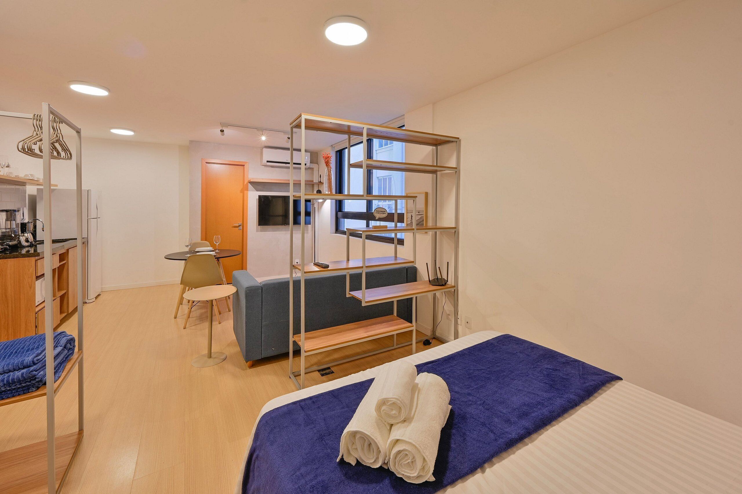 A compact hotel room with a bed, a desk, a chair, and a kitchenette.
