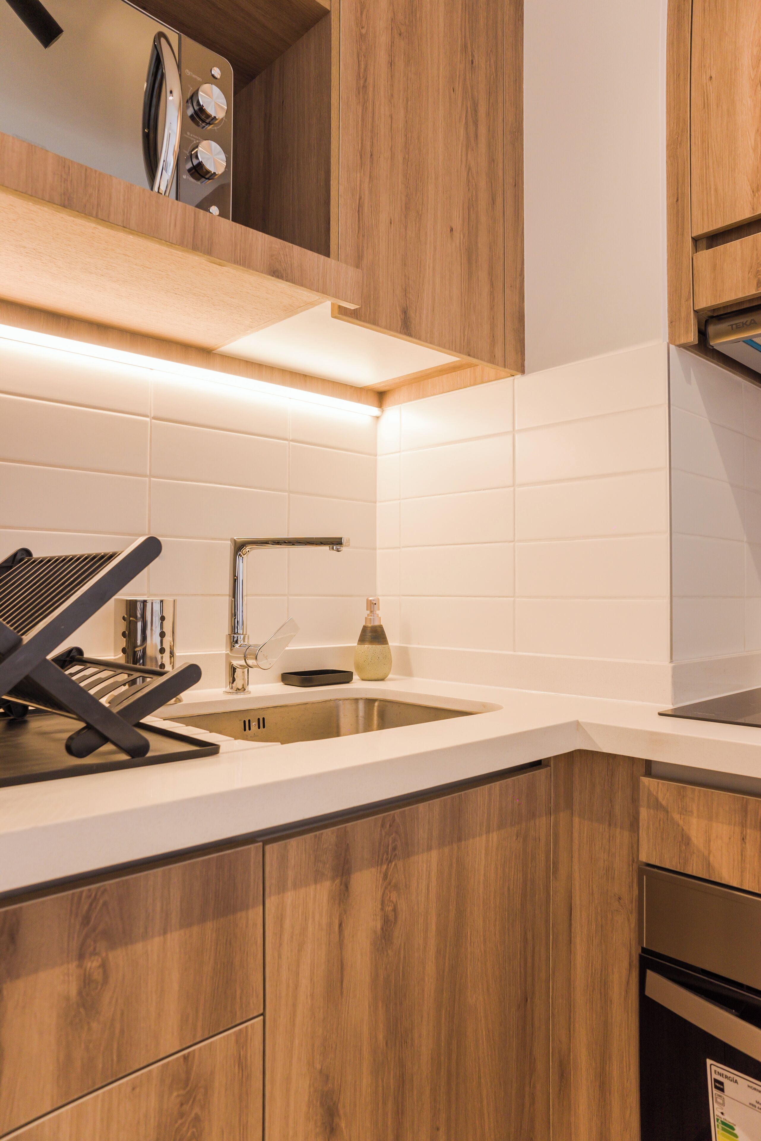 Una cocina moderna con armarios de madera, un lavamanos de acero inoxidable y un horno empotrado.