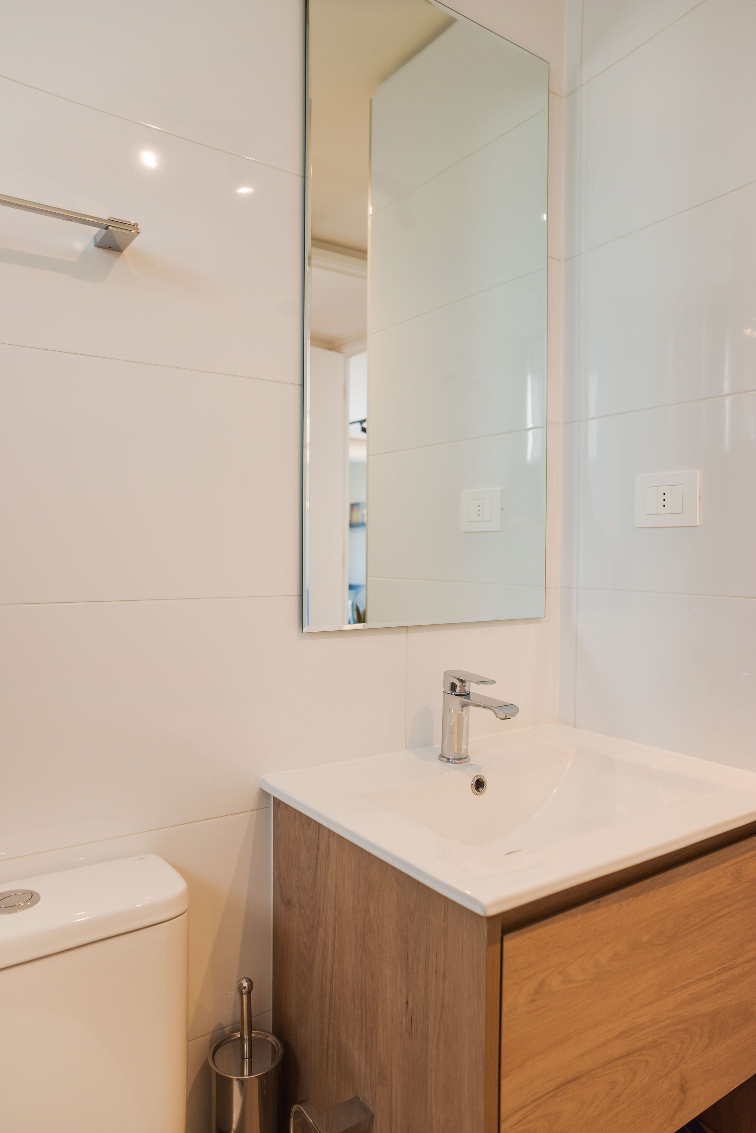 A modern bathroom with a white sink, wooden vanity, and a large mirror.