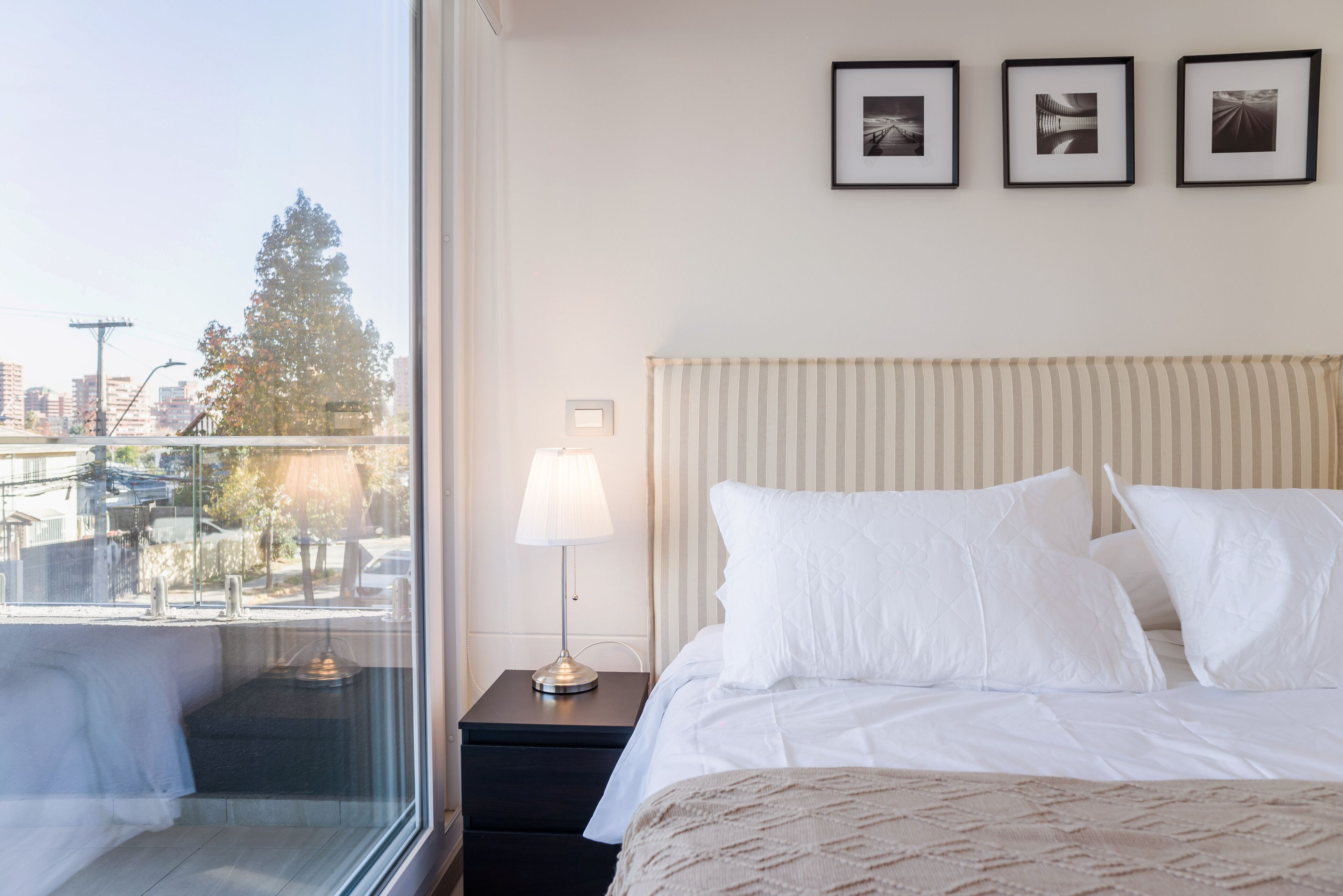 A hotel room with a bed, a nightstand with a lamp, and three framed pictures on the wall.