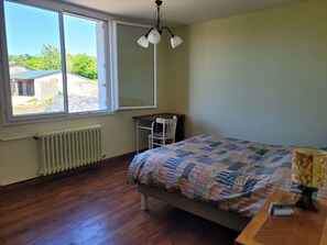 A bedroom with a bed, a desk, a chair, a radiator, and a window with a view of the outside. - Vrbo Property (Ernée)