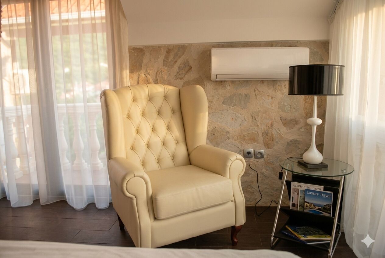 A room with a tufted armchair, a standing lamp, a small table with a book, and an air conditioning unit on the wall.
