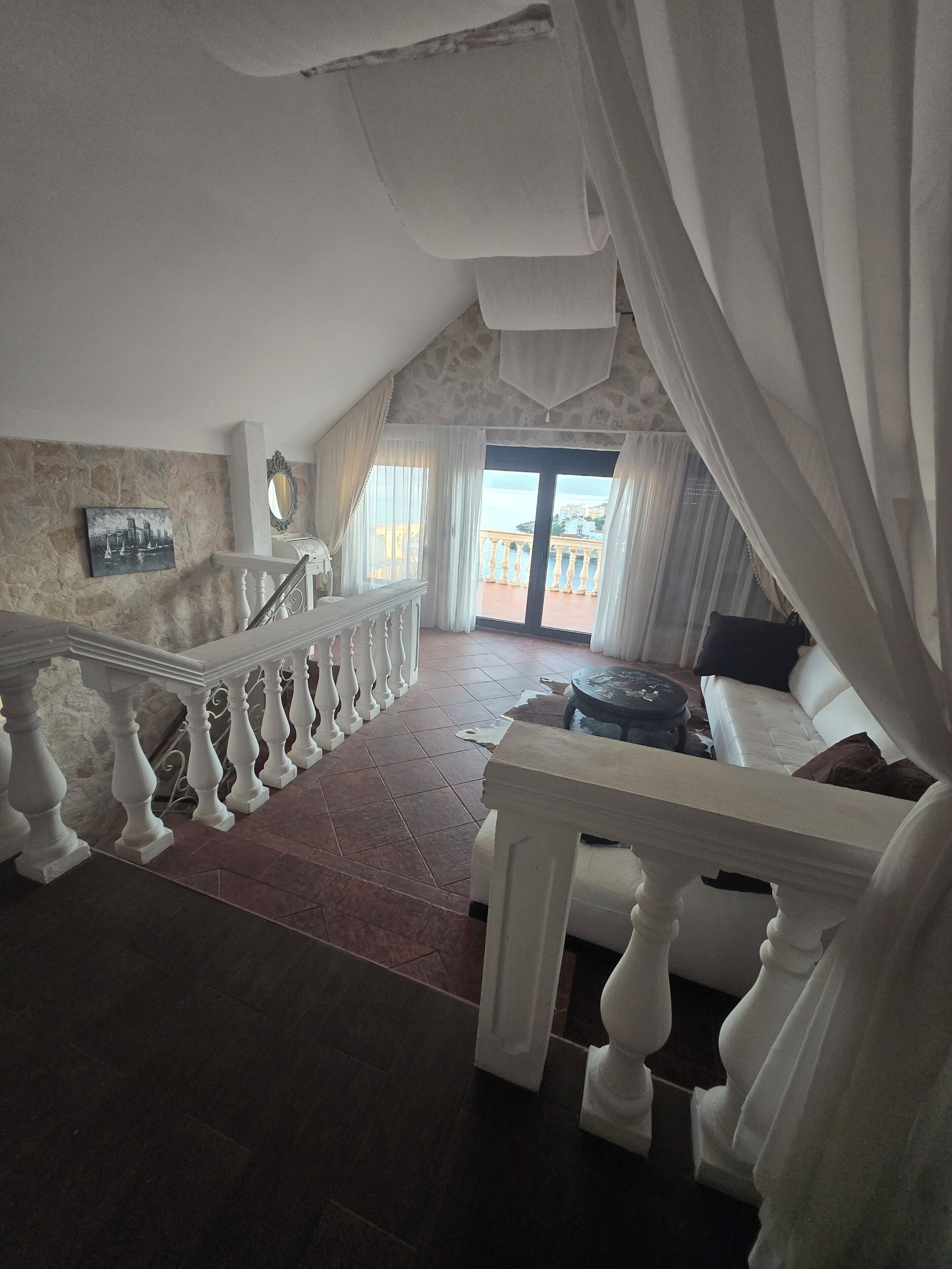Un balcon spacieux avec un mur en pierre, une balustrade blanche et une vue sur la mer.