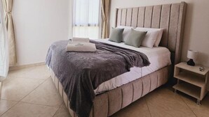 A neatly made bed with a headboard, a bedside table with a lamp, and a window with curtains.