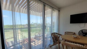 A room with a large sliding glass door, a wooden dining table with chairs, a flat-screen TV mounted on the wall, and a view of a grassy area outside.