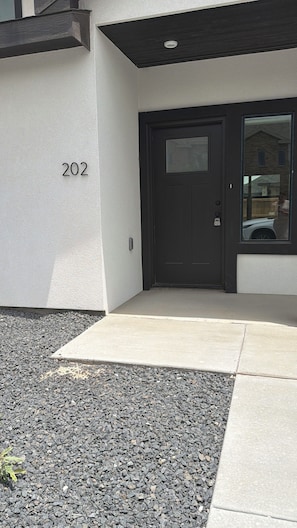 A building entrance with a dark-colored door, a small window, and a number '202' on the wall. - Modern Montana Hideaway (Odessa)