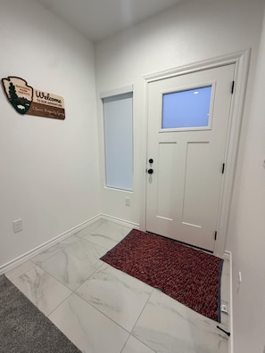 A clean, white-walled hallway with a wooden welcome sign, a white door with a window, and a red carpet leading to the door. - Modern Montana Hideaway (Odessa)
