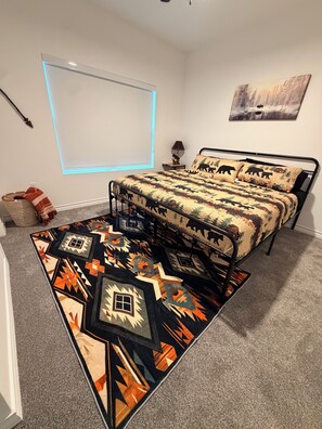 A bedroom with a bed, a window with blinds, a rug, and a wall-mounted lamp. - Modern Montana Hideaway (Odessa)