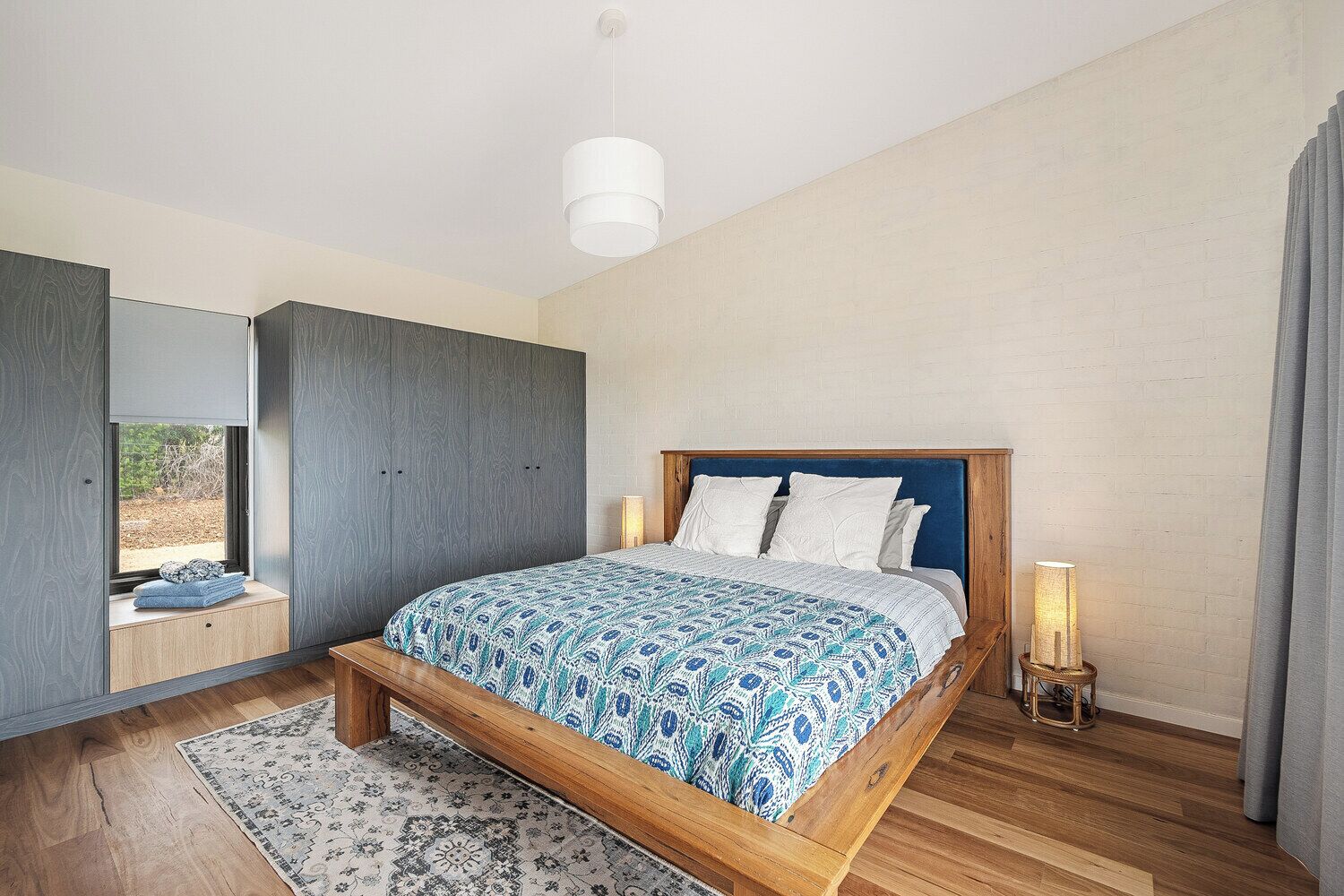 A modern bedroom with a wooden bed, a large window, and a built-in wardrobe.