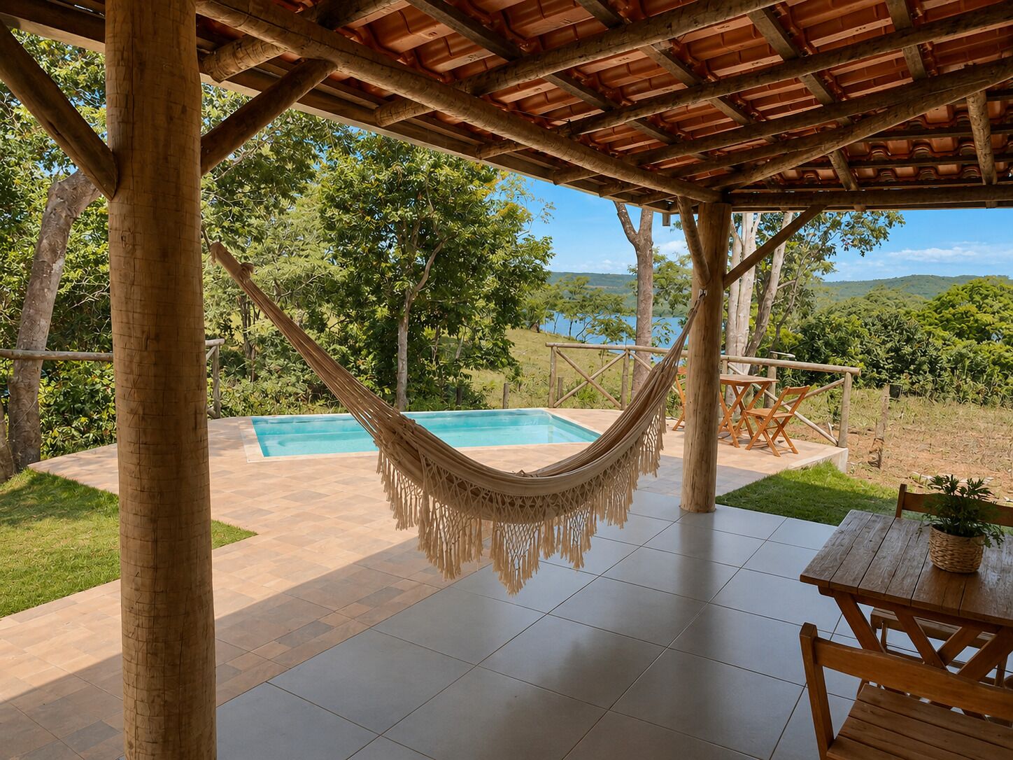 A covered outdoor area with a hammock, a pool, and a wooden table with chairs.