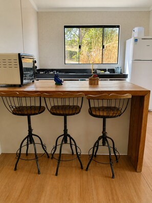 A kitchen with a wooden island, three metal chairs, a toaster, a refrigerator, and a window with a view of trees.