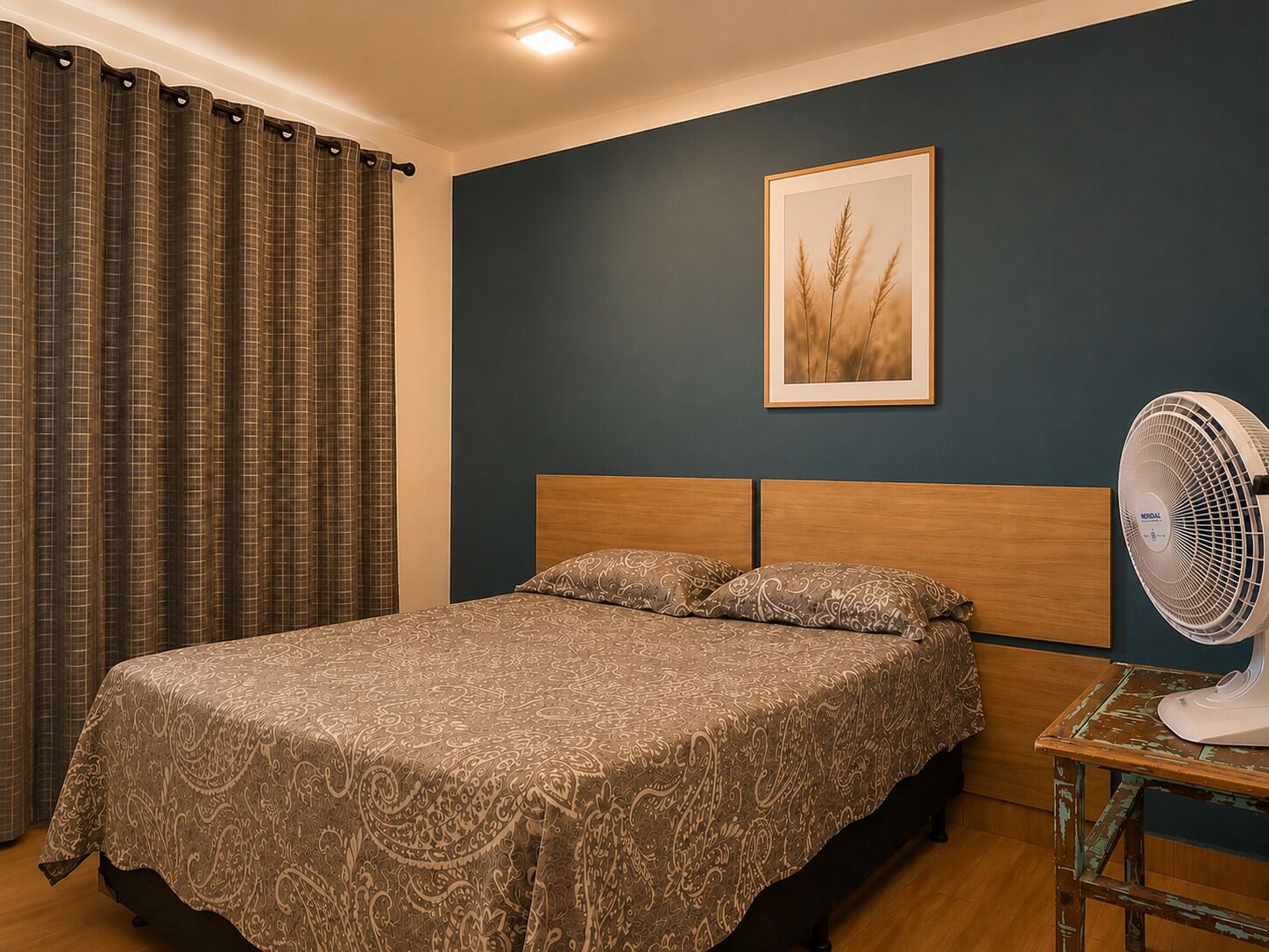 A bedroom with a bed, curtains, a wall-mounted fan, and a framed picture.