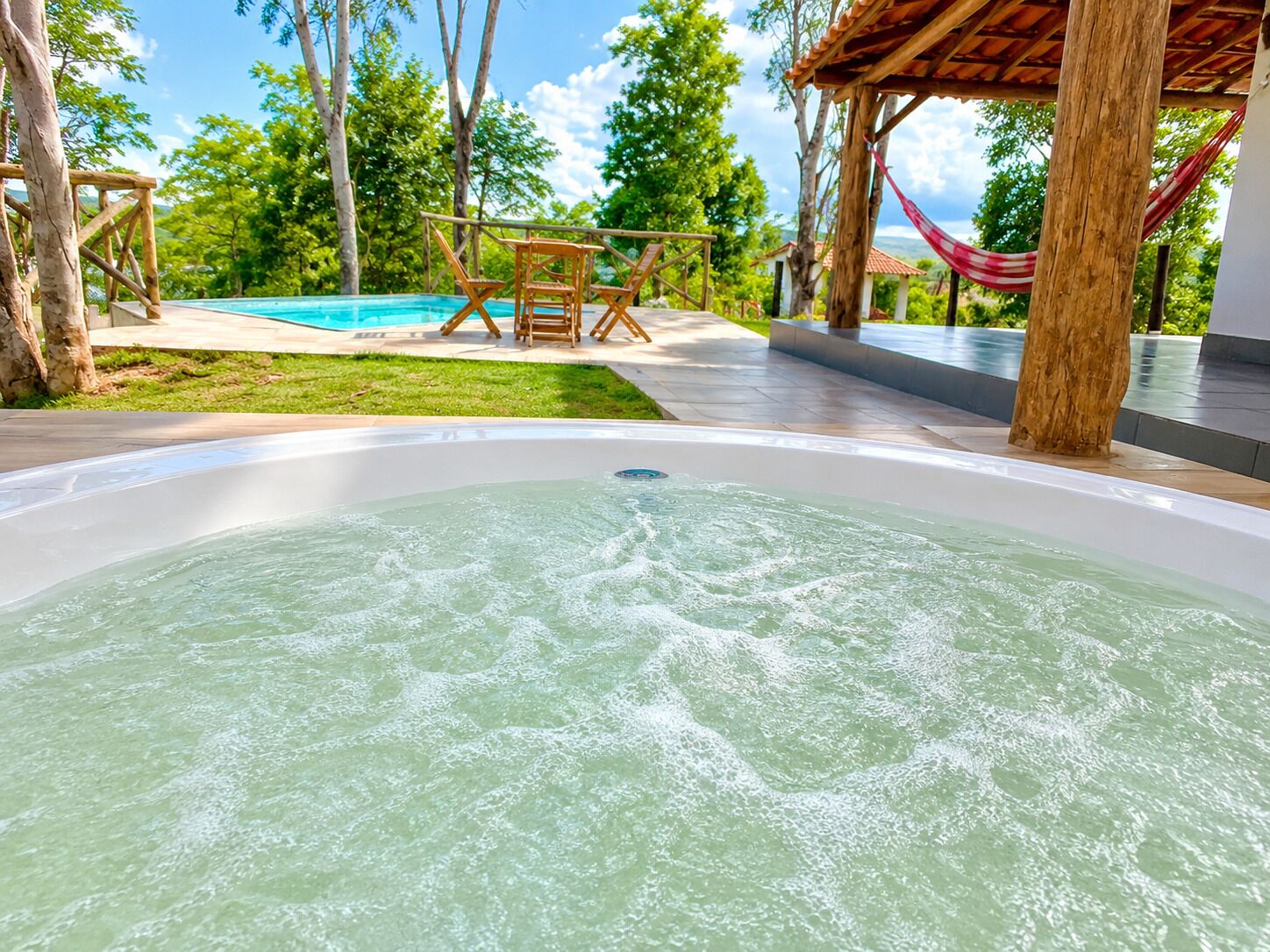 A hot tub with a view of a pool and a hammock.