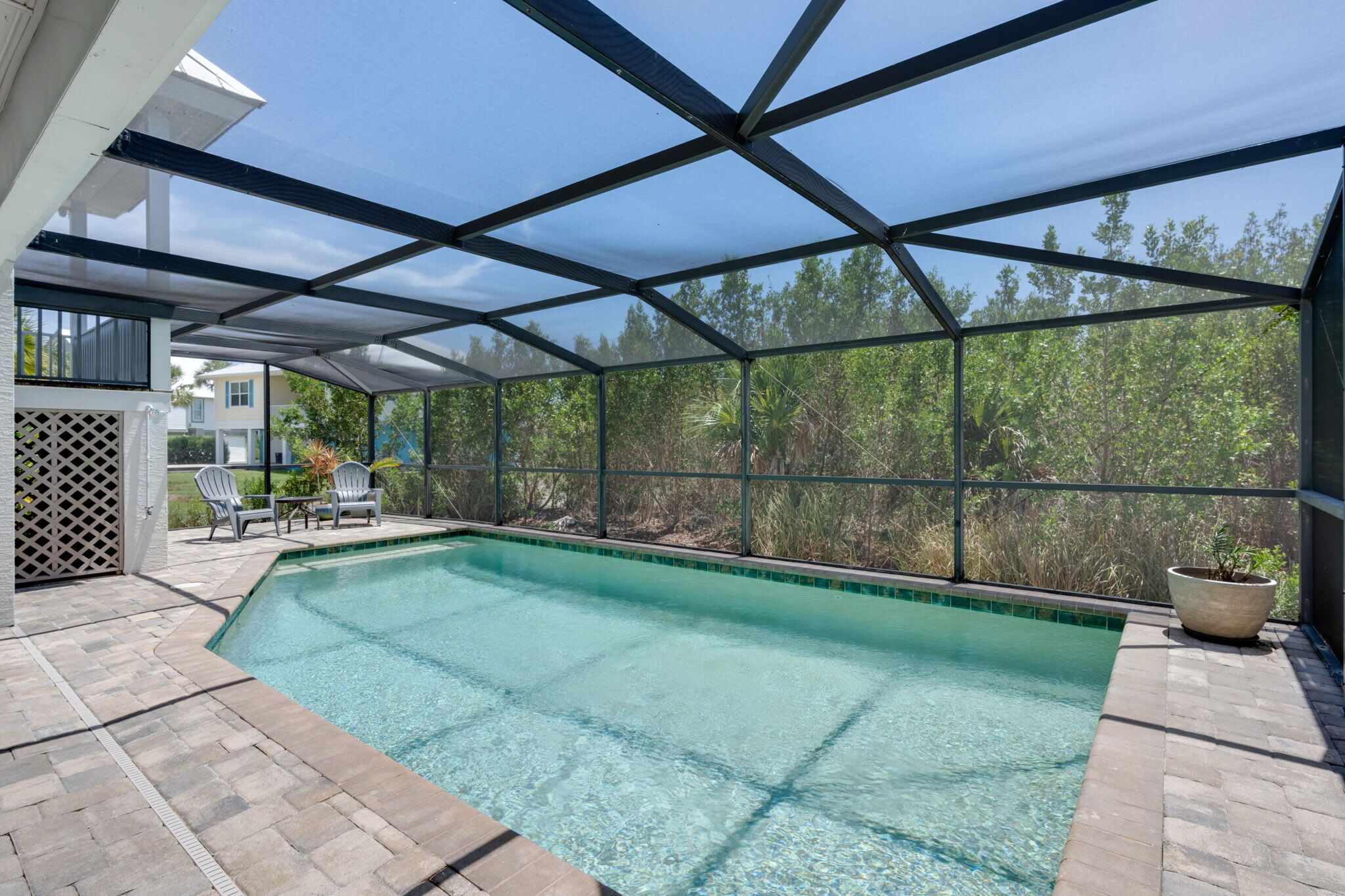 Une piscine dotée d’un patio couvert, entourée d’arbres et offrant une vue sur un ciel dégagé.