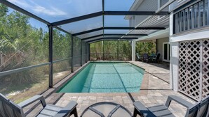 A covered outdoor swimming pool with a patio area, surrounded by a house and vegetation. - Charming pool home in Sea Oats, Sanibel Island (Sanibel)