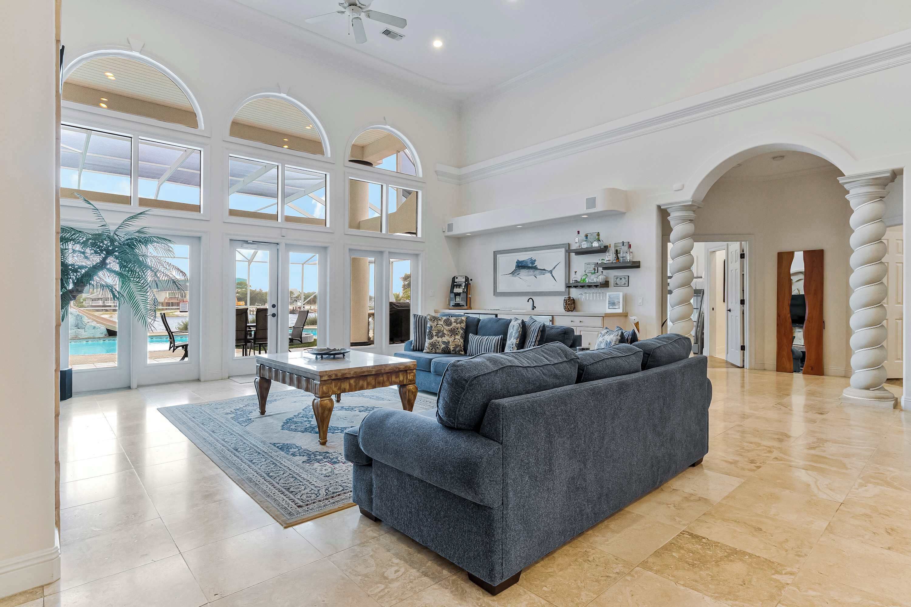 Un salon spacieux avec un grand canapé gris, une table basse et une vue sur une piscine, visible à travers de grandes fenêtres.