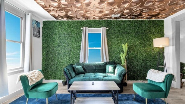 Una habitación con un sofá verde, dos sillones verdes, una mesa de centro, un techo con estampado floral y una pared verde.