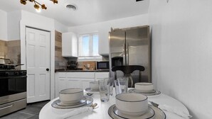 Una cocina moderna con armarios blancos, un refrigerador de acero inoxidable y una mesa de comedor con platos, tazones y vasos.