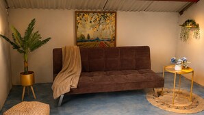 A room with a brown sofa, a round wooden table with a vase, a potted plant, and a painting on the wall.