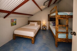 Ein Zimmer mit einem Etagenbett und einem Einzelbett, beide mit Holzrahmen. Es gibt einen kleinen Nachttisch mit einer Lampe und einer Blumenvase.