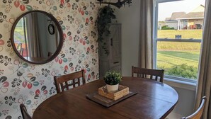 A dining area with a round table, chairs, a mirror, and a window with a view of houses.